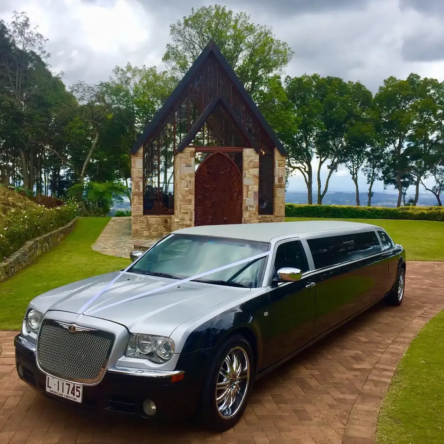 Black and silver limousine parked on brick pathway near a chapel with scenic green background.  — Superstretch300 Limousines in Mooloolaba, QLD