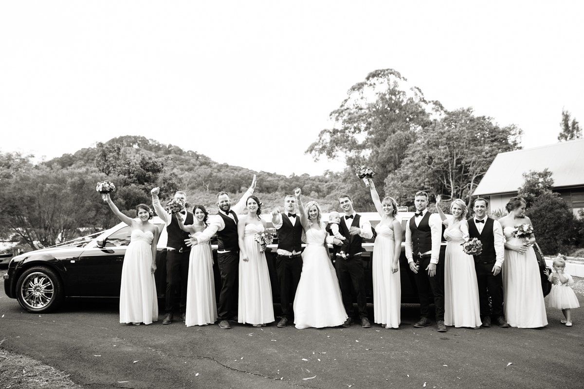 A Black and White Photo of a Wedding Party Standing in Front of a Car — Superstretch300 Limousines in Sunshine Coast, QLD