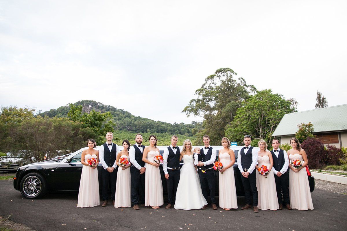 The Bride and Groom Are Posing for a Picture in Front of a Black Car — Superstretch300 Limousines in Sunshine Coast, QLD