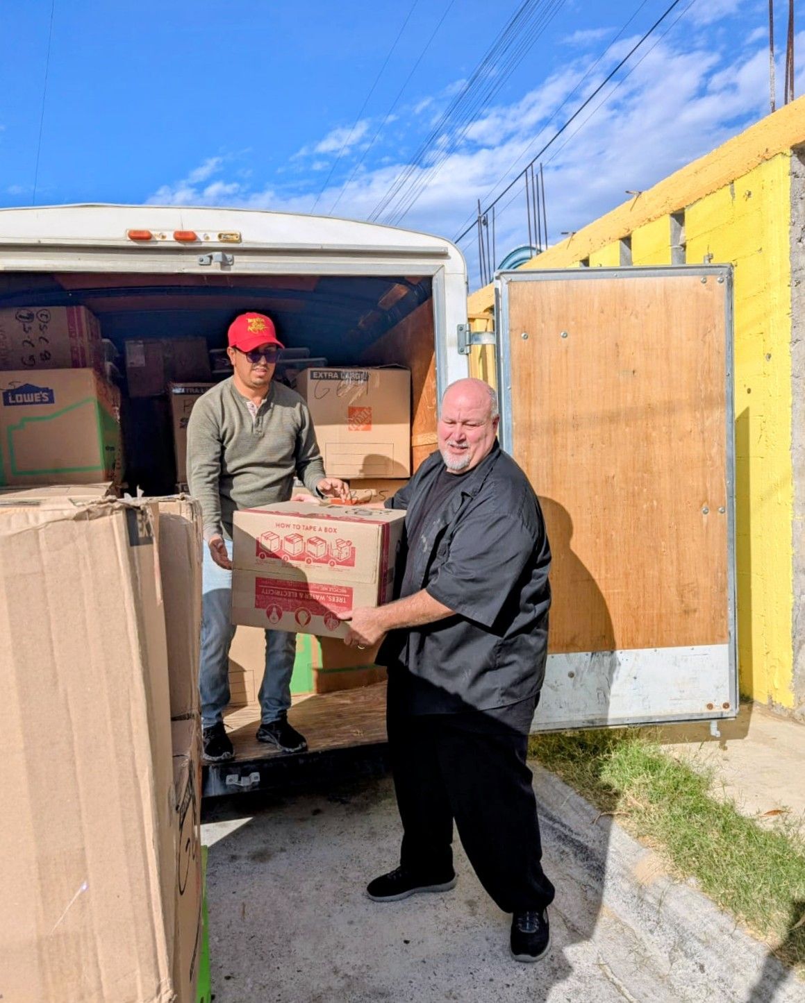Boxes in a trailer being loaded by several people standing near stairs.