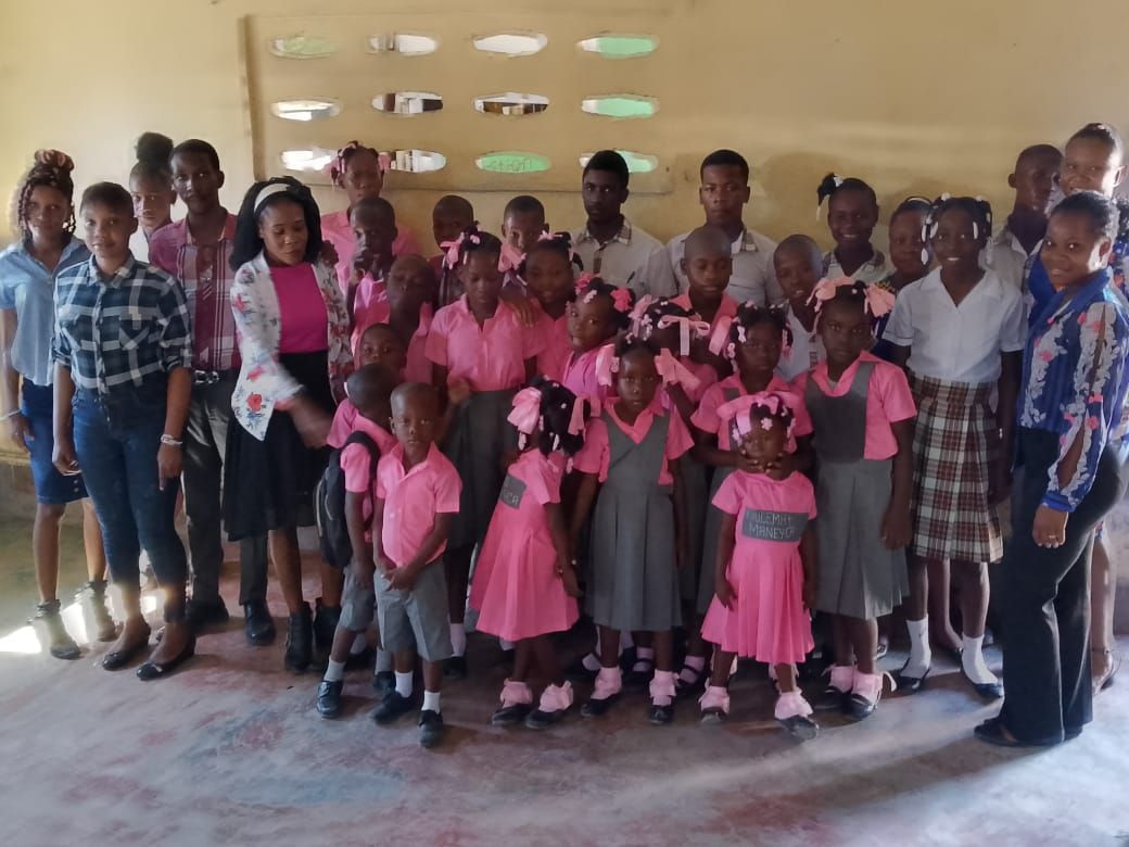 Group of children in pink uniforms with adults in a classroom setting.