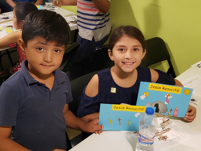 Two children holding colorful artwork, one saying