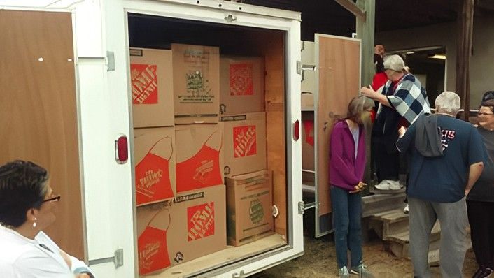 Boxes in a trailer being loaded by several people standing near stairs.