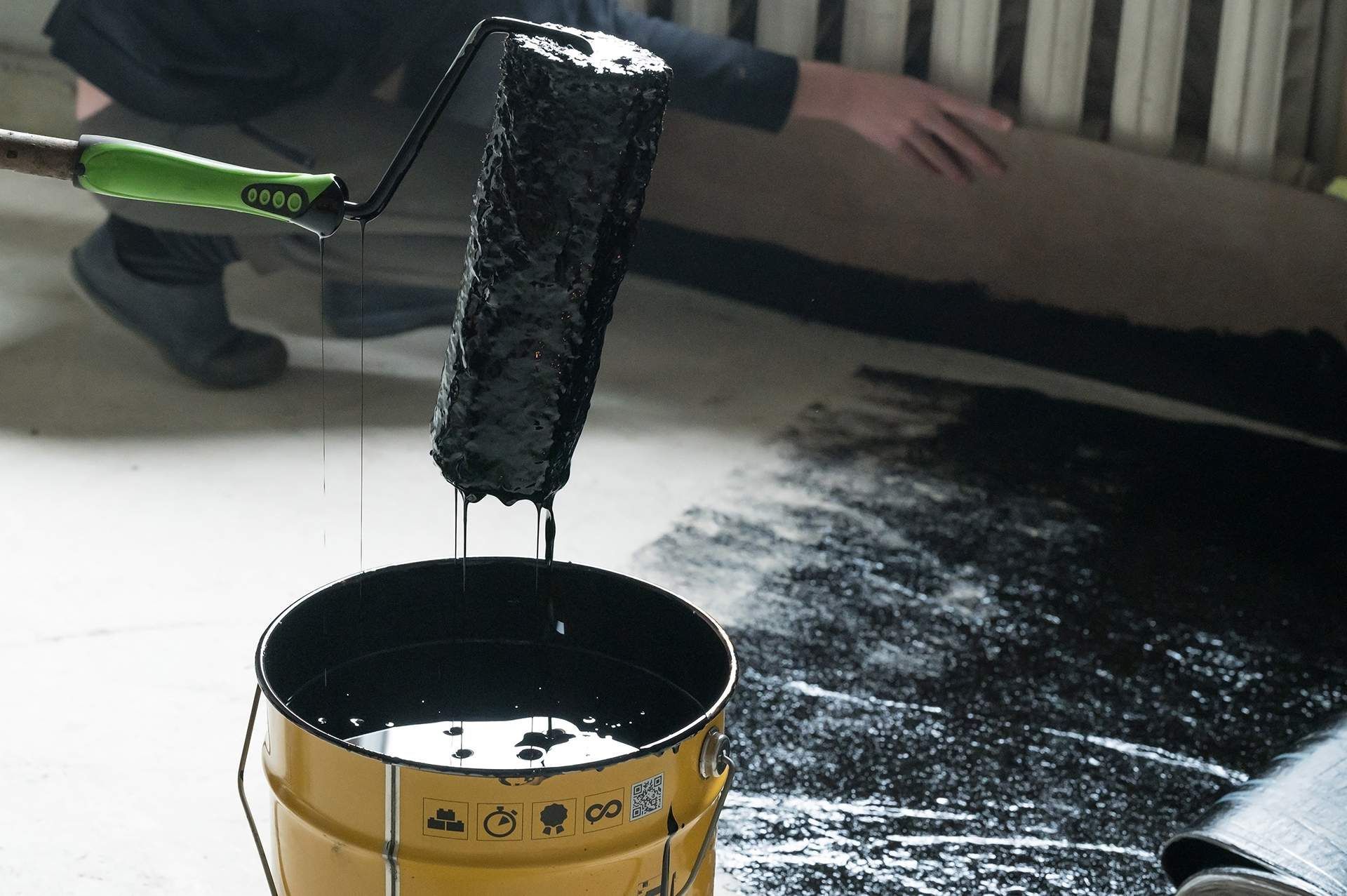 Applying hot resin to the floor for waterproofing, roller and bucket of resin, black and liquid resin