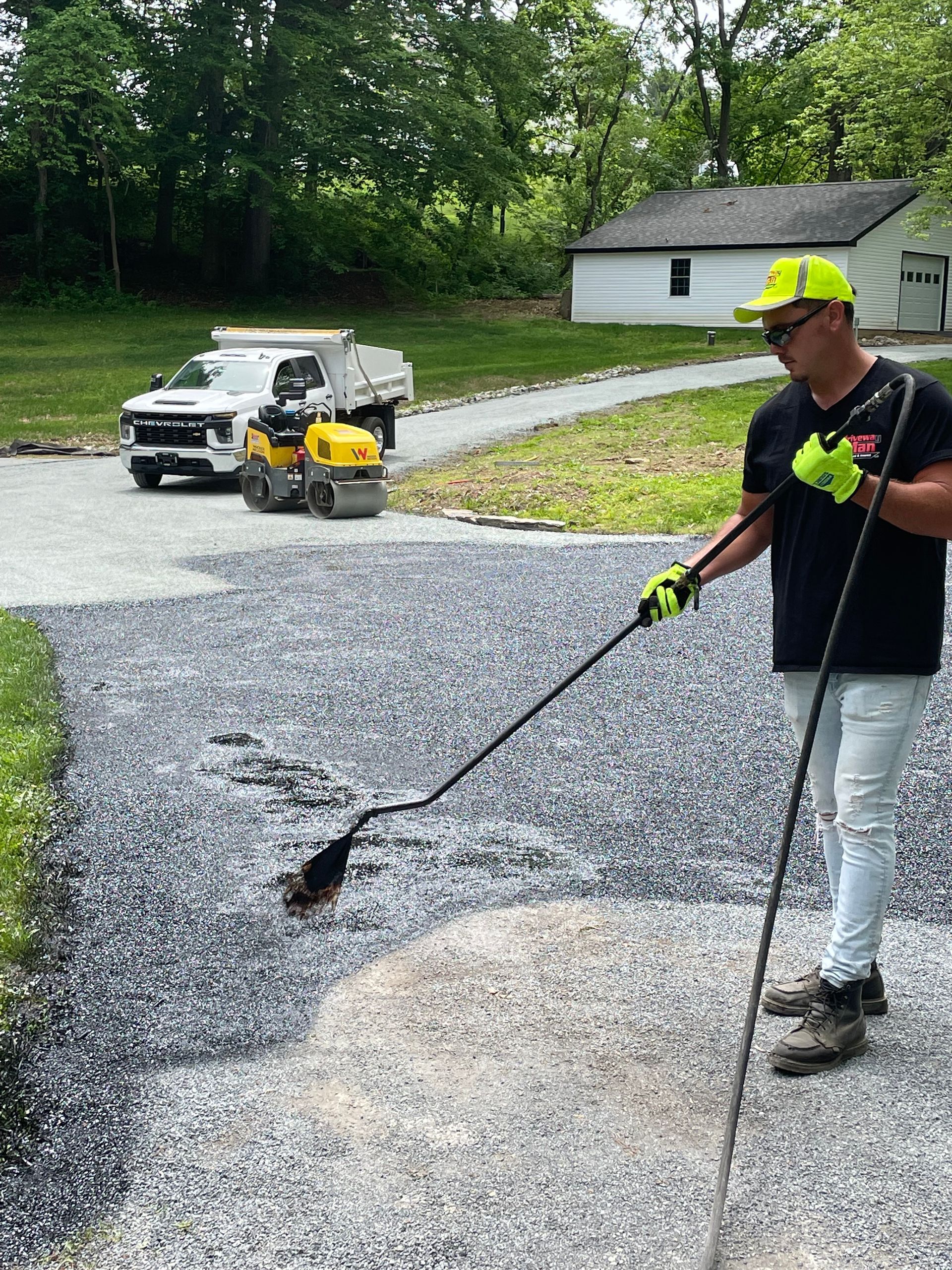A man is spreading asphalt on a driveway with a broom.