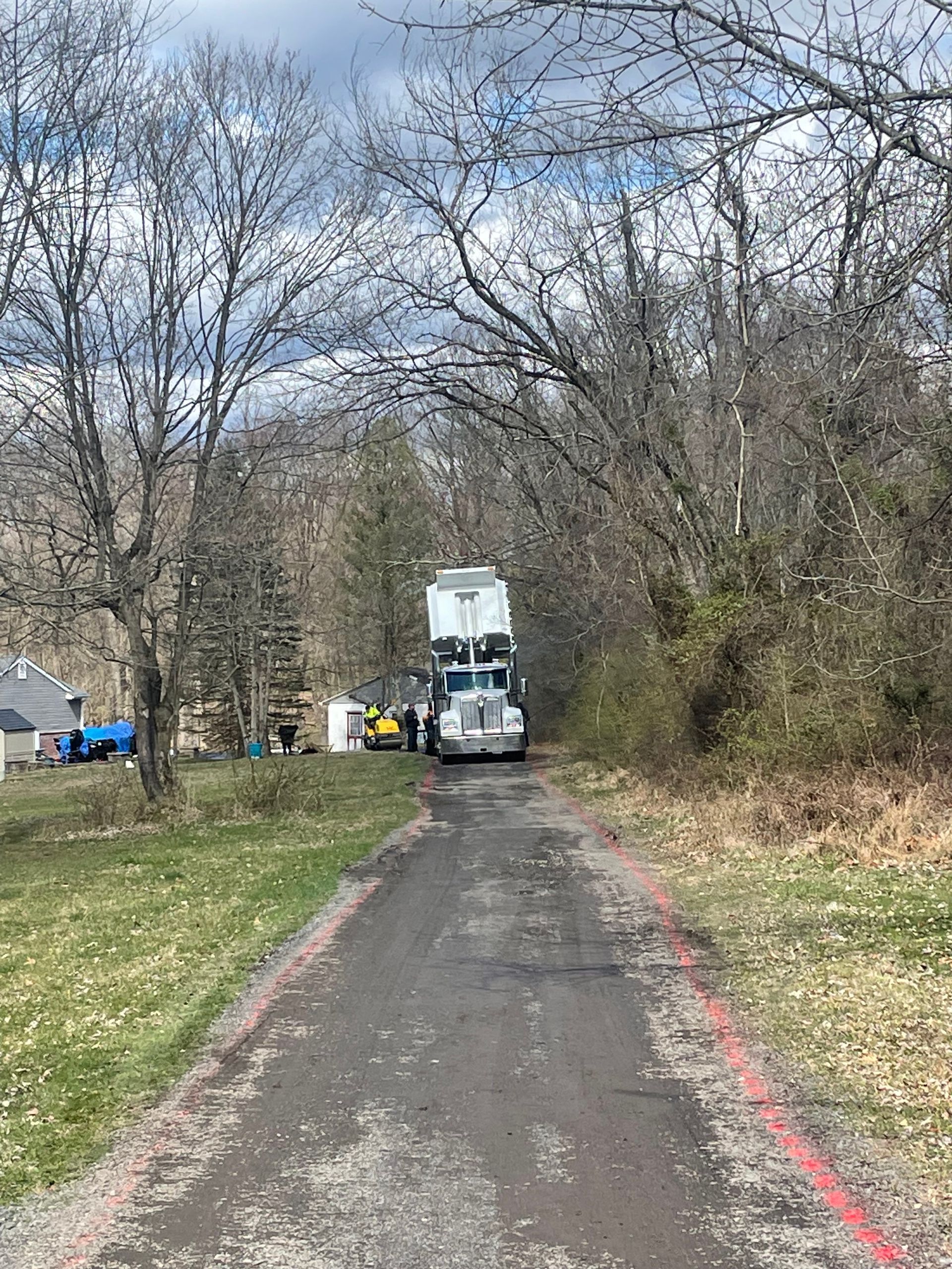 A semi truck is driving down a dirt road next to trees.