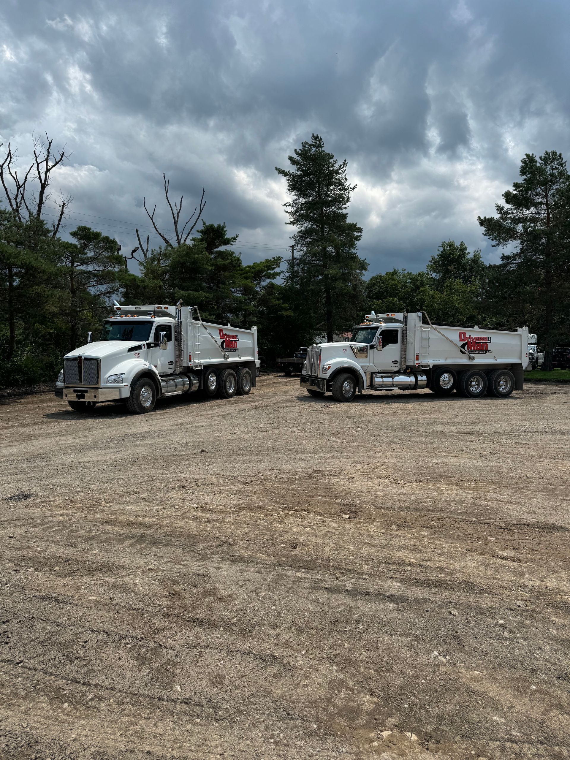 Two dump trucks are parked in a gravel lot