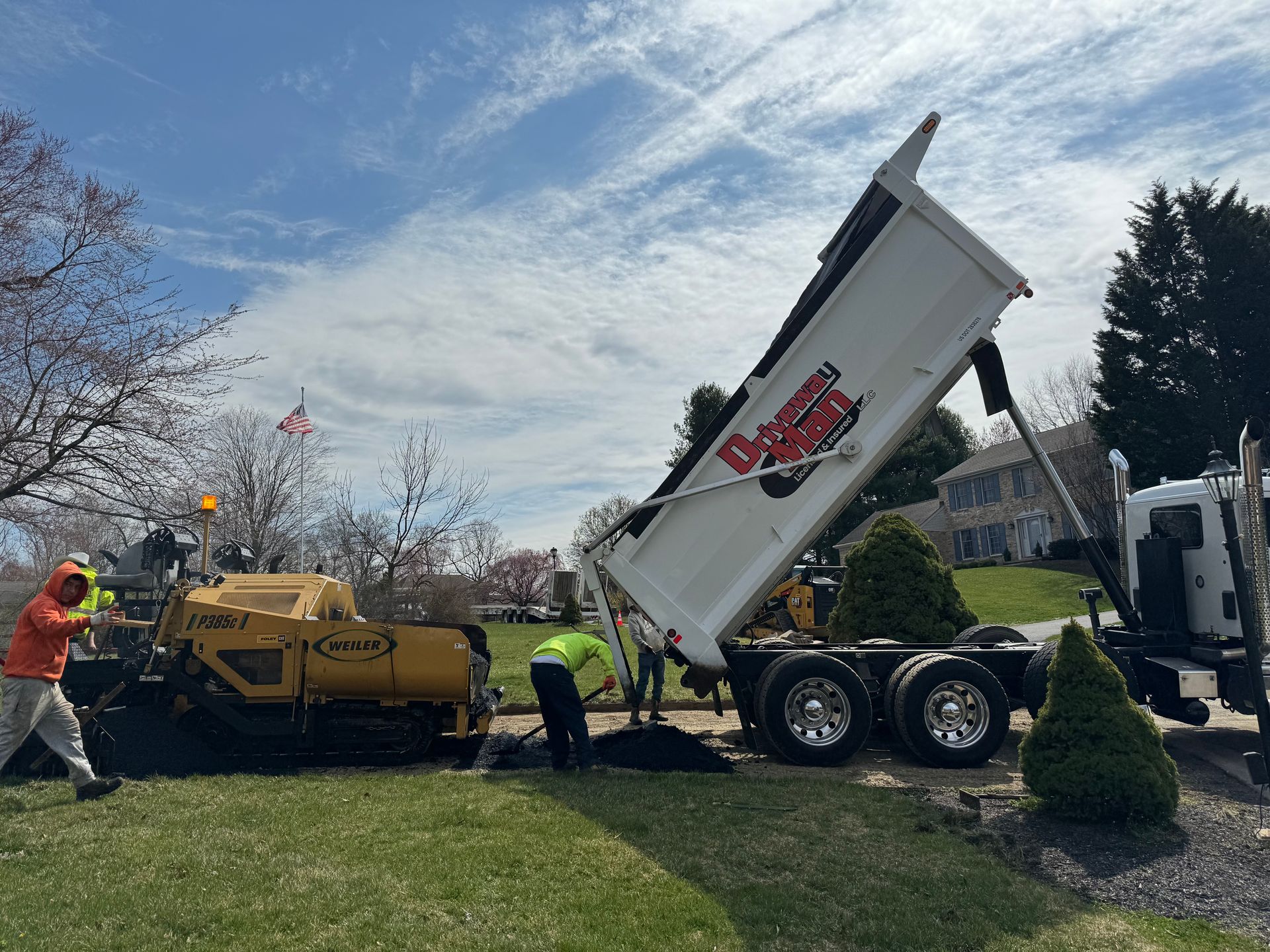 A dump truck is being loaded with asphalt in a yard.