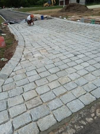 A man is kneeling down on a brick driveway.