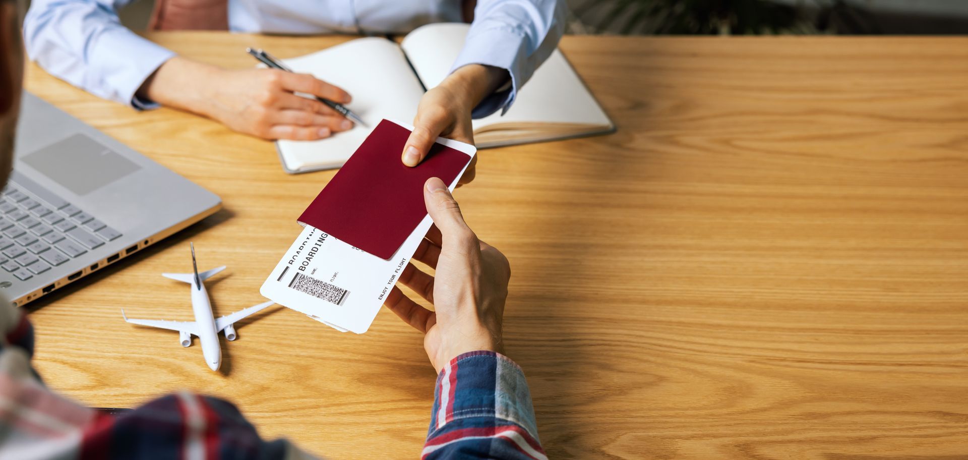 Person receiving passport and boarding pass across a desk with laptop and model airplane. Person receiving passport and boarding pass across a desk with laptop and model airplane.
