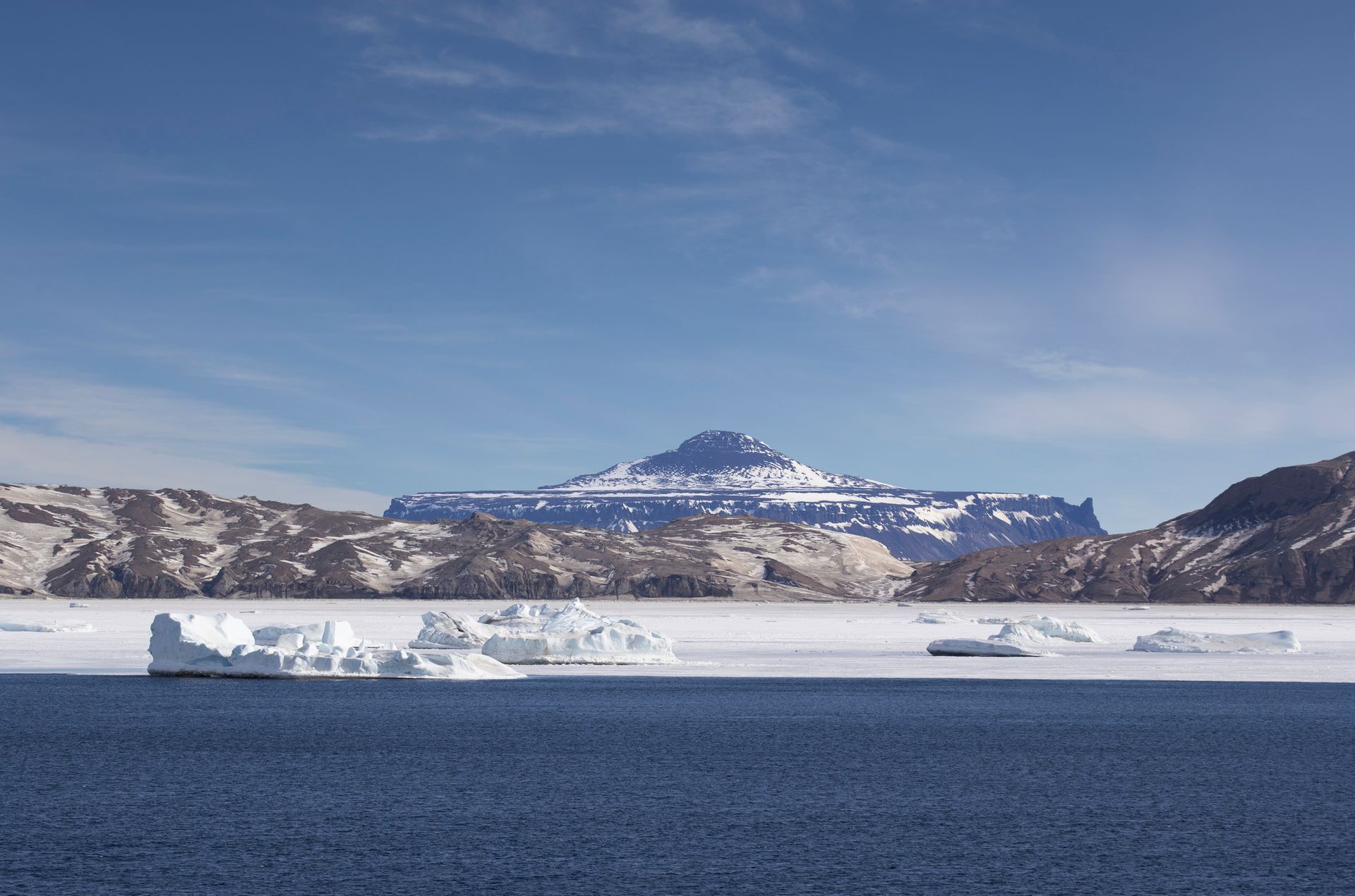 A large iceberg in the middle of a body of water with mountains in the background