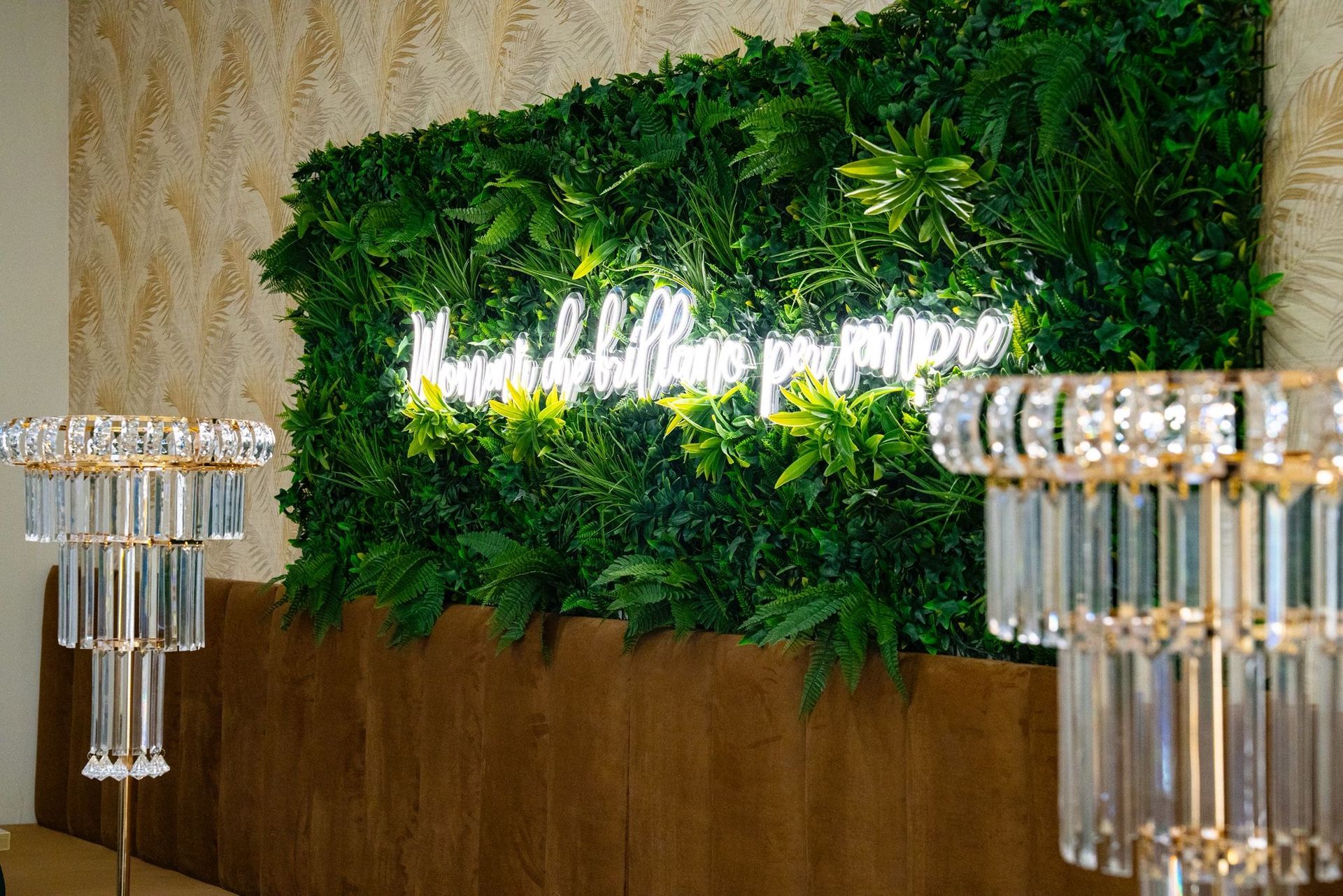 L'interno di un locale caratterizzato da tavoli con sedie in velluto verde, centrotavola in cristallo e un'insegna al neon