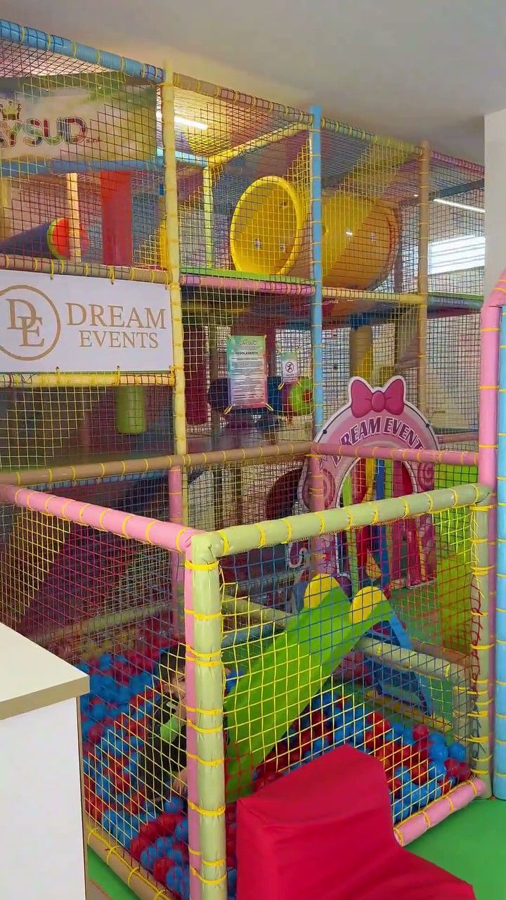 Una struttura di gioco multilivello per bambini, con piscina di palline, scivolo, reti per arrampicata e tubi di plastica.