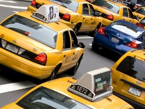 Yellow taxi roof sign with "TAXI" in black letters; cityscape background.