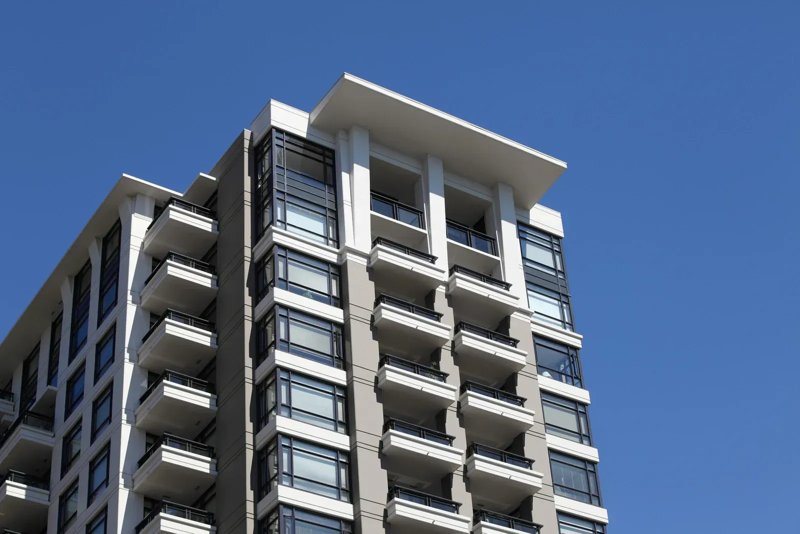 Modern high-rise apartment building against a clear blue sky. Balconies and large windows are visible.