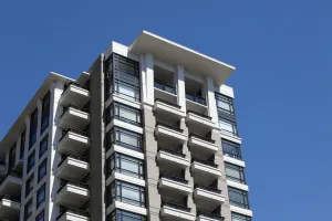 Modern high-rise apartment building against a clear blue sky. Balconies and large windows are visible.