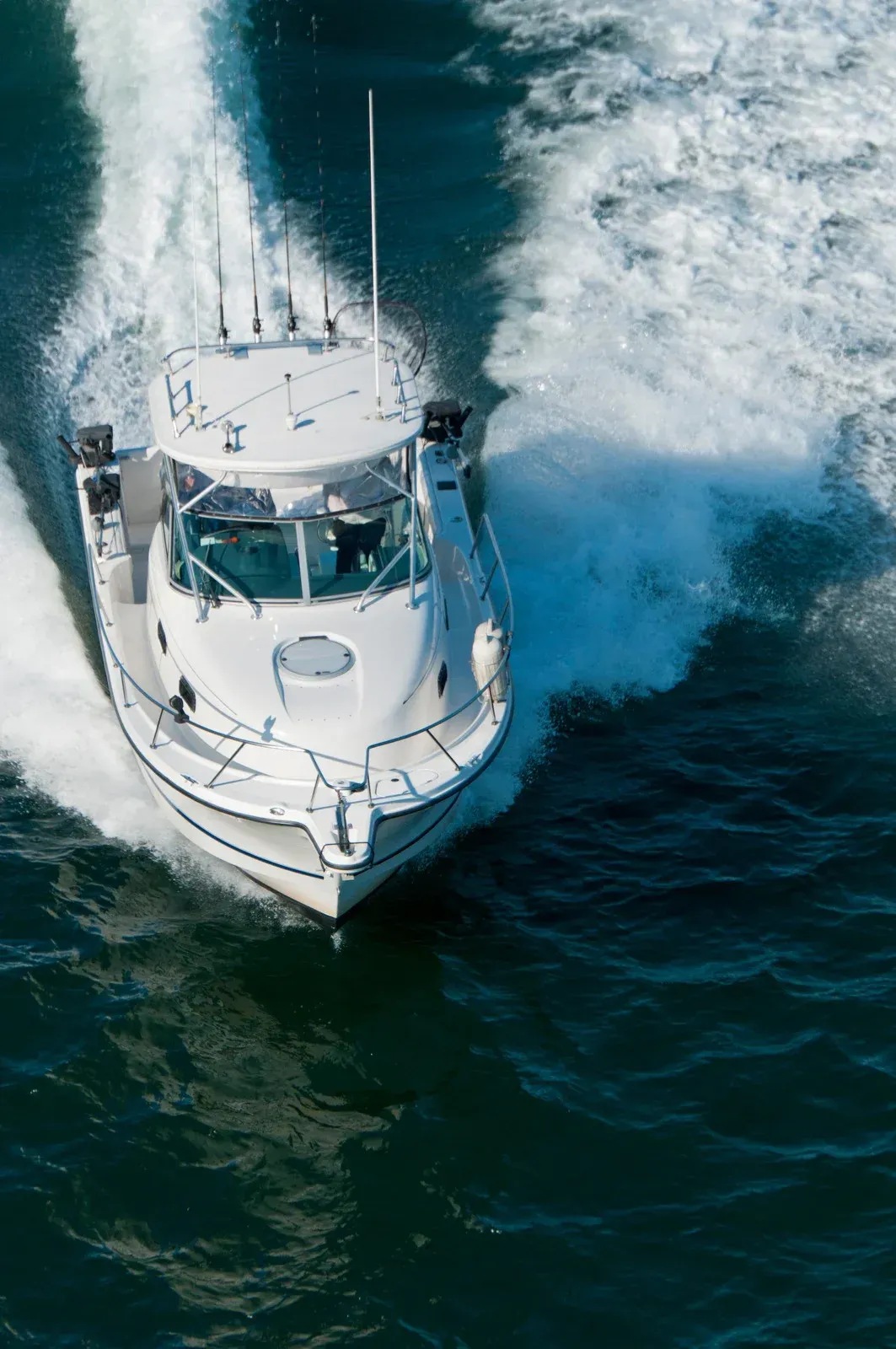 White motorboat speeding across dark blue water, creating white wakes.