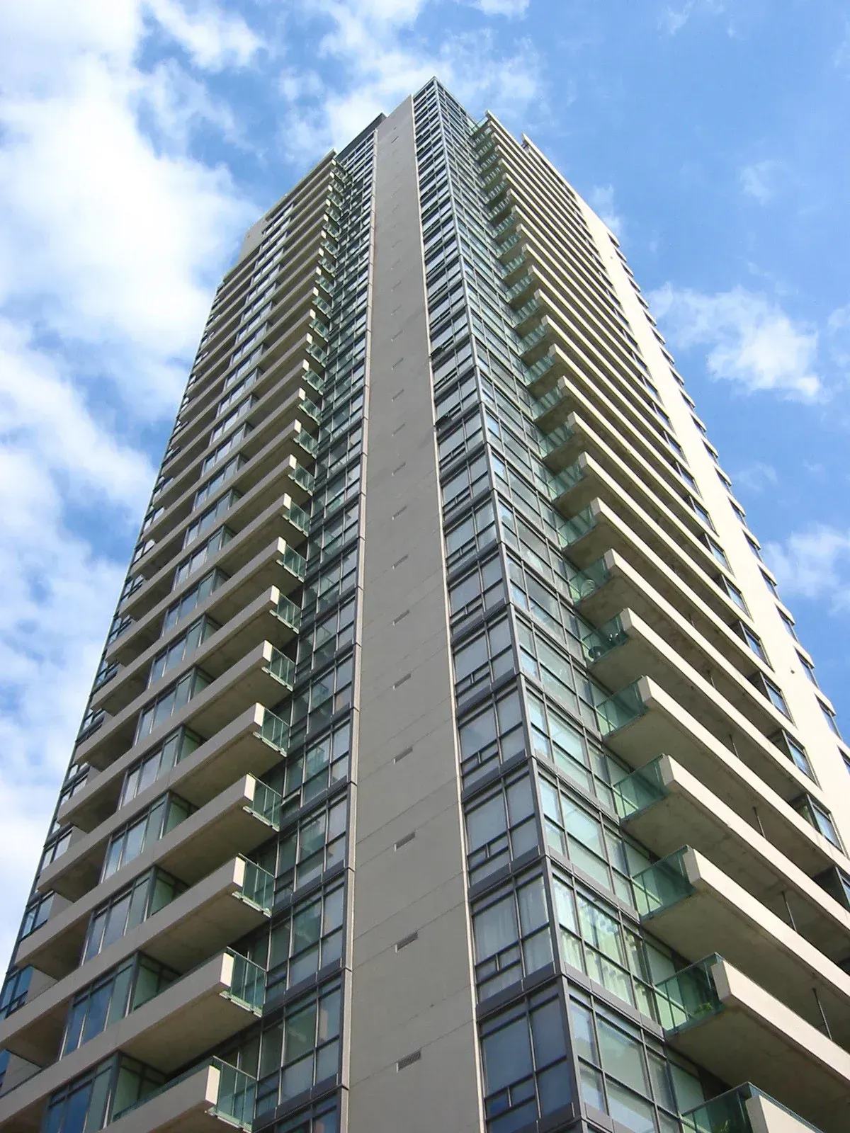 Tall, modern apartment building with balconies against a blue sky.