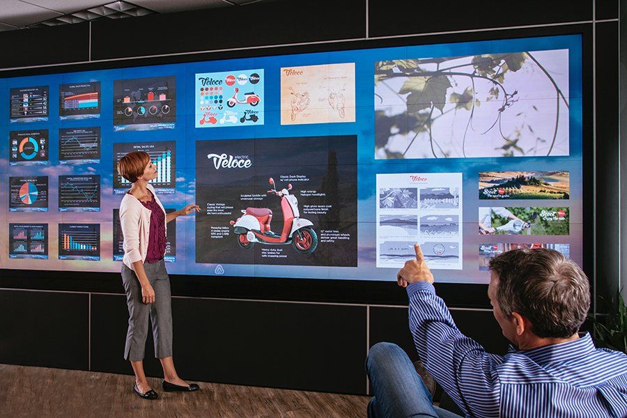 A man and a woman are standing in front of a large screen.