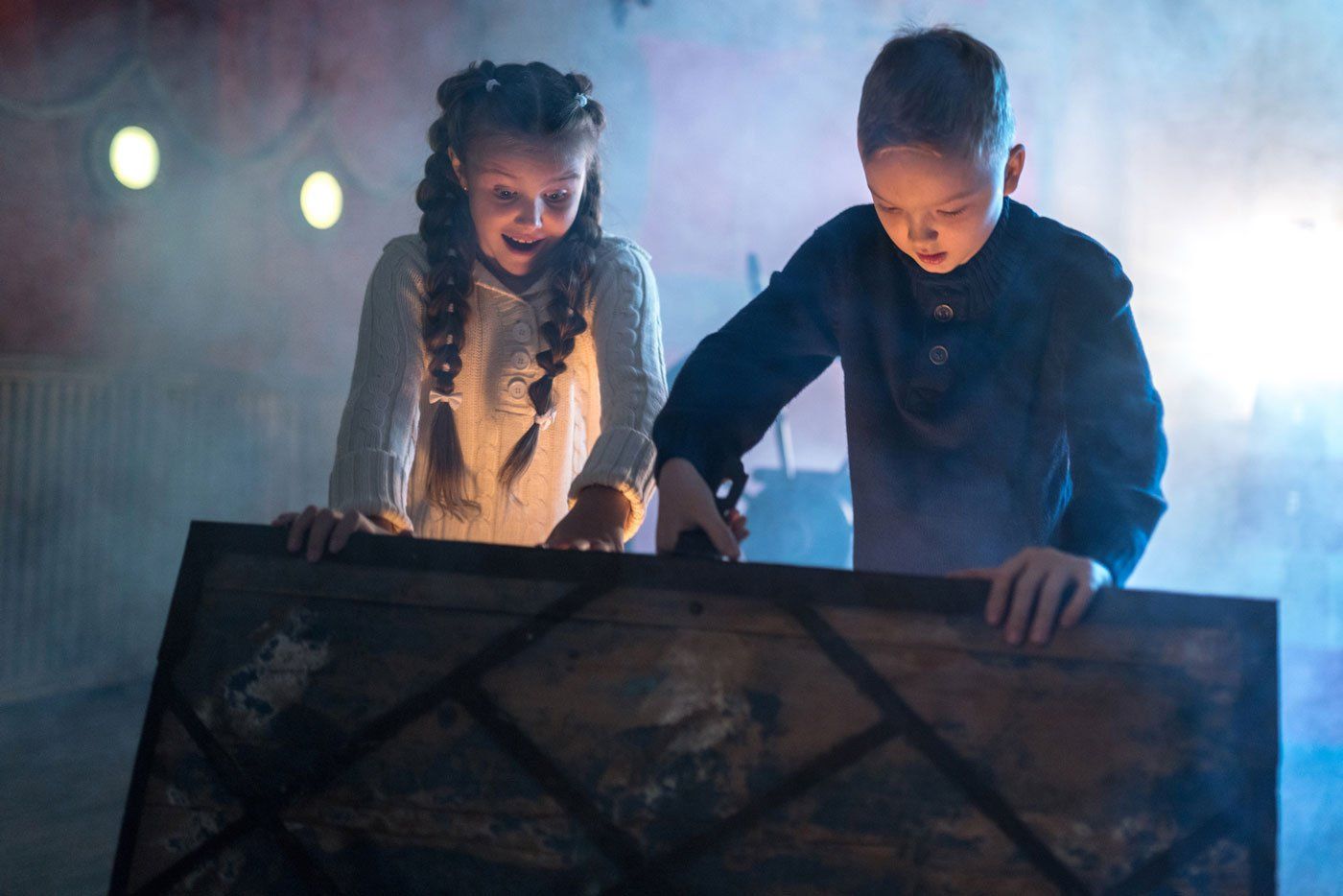 A boy and a girl are looking into a trunk in a dark room.