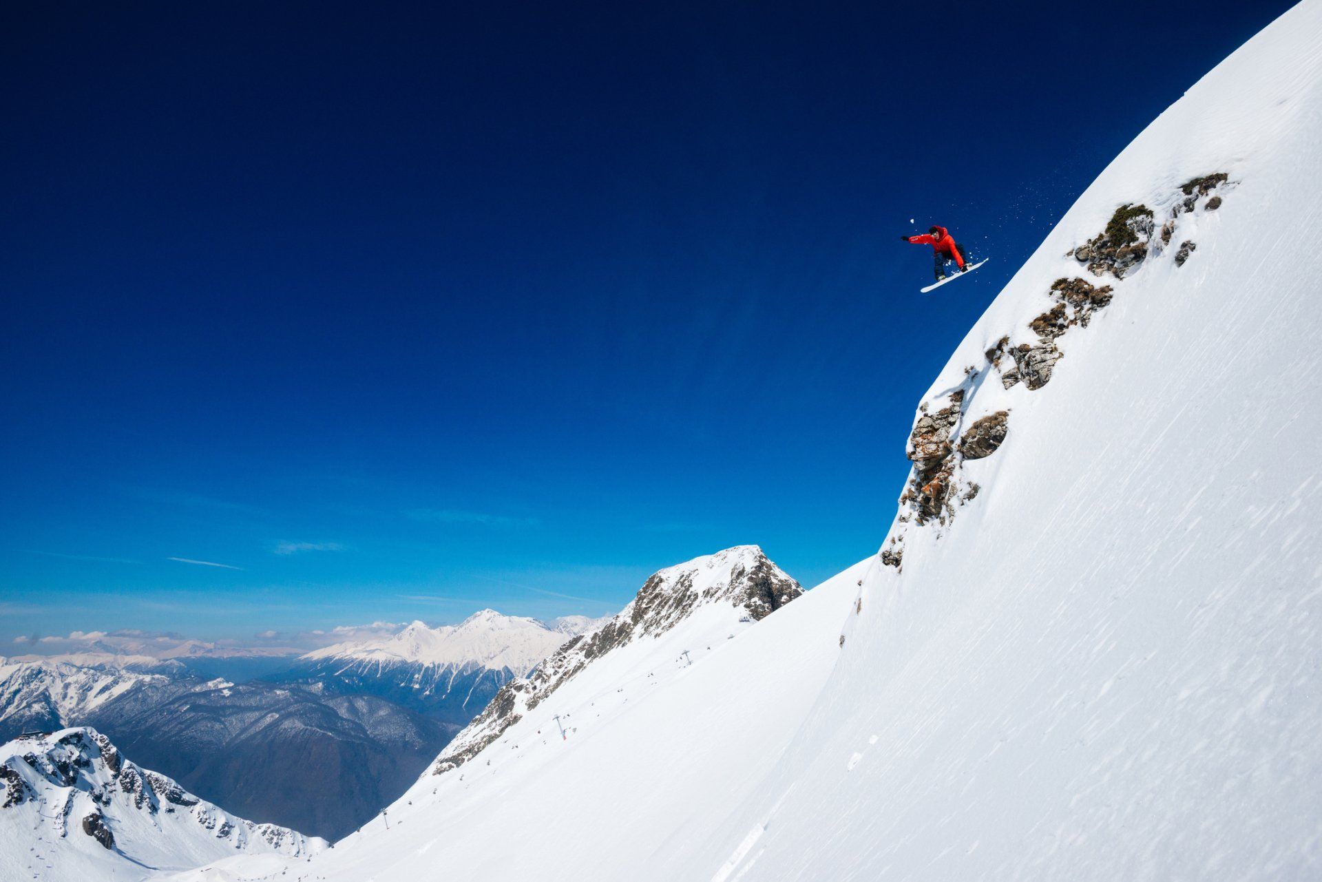 A snowboarder is doing a trick on top of a snow covered mountain.