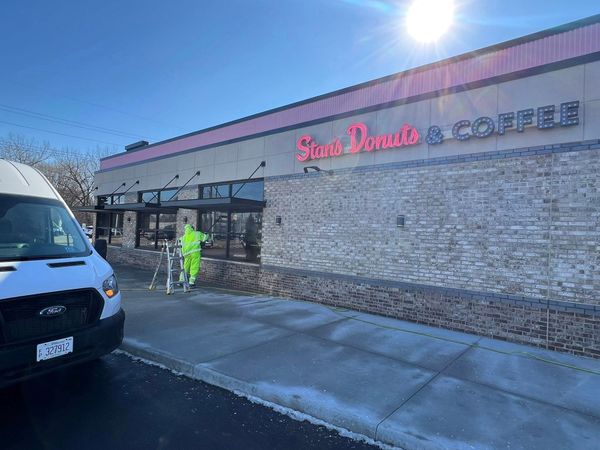 Exterior of a coffee shop with stone facade, pink and gray signage, and a worker in neon safety gear outside