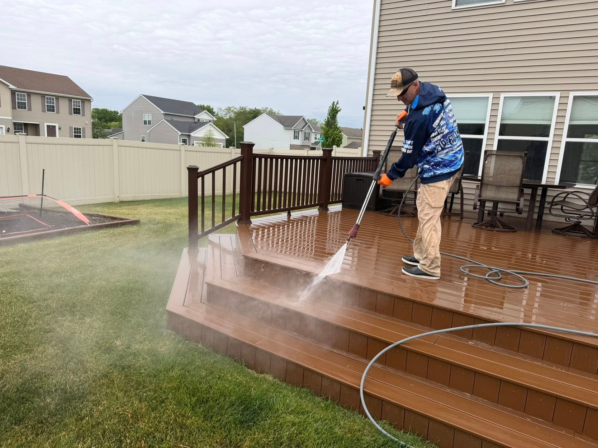 Person pressure-washes a wet wooden deck beside a backyard lawn.