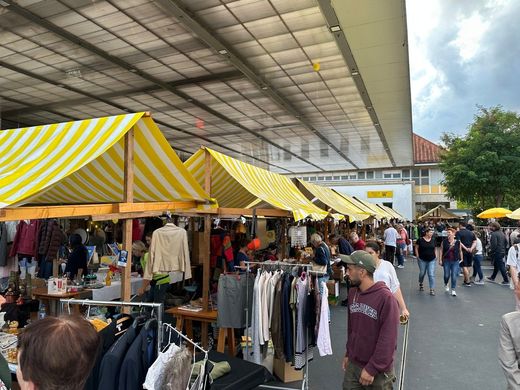 Freiluftmarkt mit gelb gestreiften Ständen und Käufern unter einem großen Dach