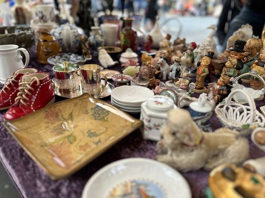 Verschiedene Antiquitäten und Keramikfiguren lagen auf einem überfüllten Markttisch neben Tellern und Teekannen.