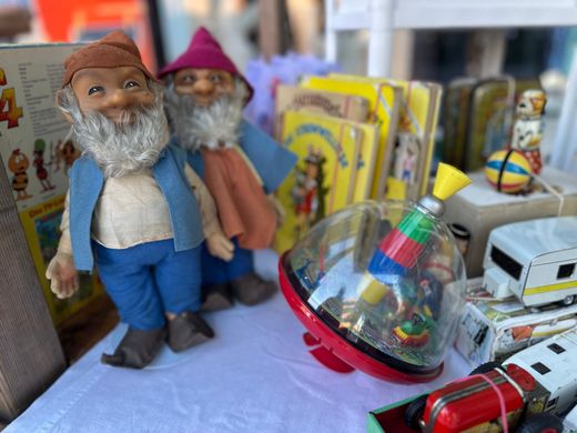 Zwei Gartenzwergfiguren neben Spielzeugautos und einem bunten Kreisel auf einem Regal.