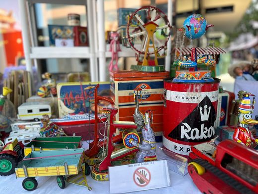 Bunte, alte Spielzeuglastwagen und rote Metallfässer sind auf einem Tisch in einem Schaufenster ausgestellt.