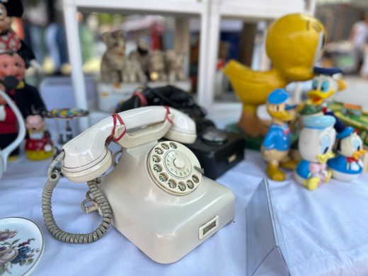 Ein antikes Wählscheibentelefon auf einem Tisch, im Hintergrund kleine Figuren und eine gelbe Ente.
