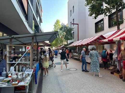 Marktstraße im Freien mit Käufern und gestreiften Markisen neben Cafés und Verkaufsständen