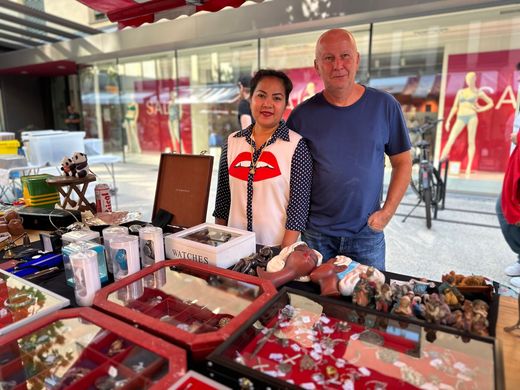 Zwei Personen hinter einem Marktstand, an dem verpackte Lebensmittel und Süßigkeiten angeboten werden.