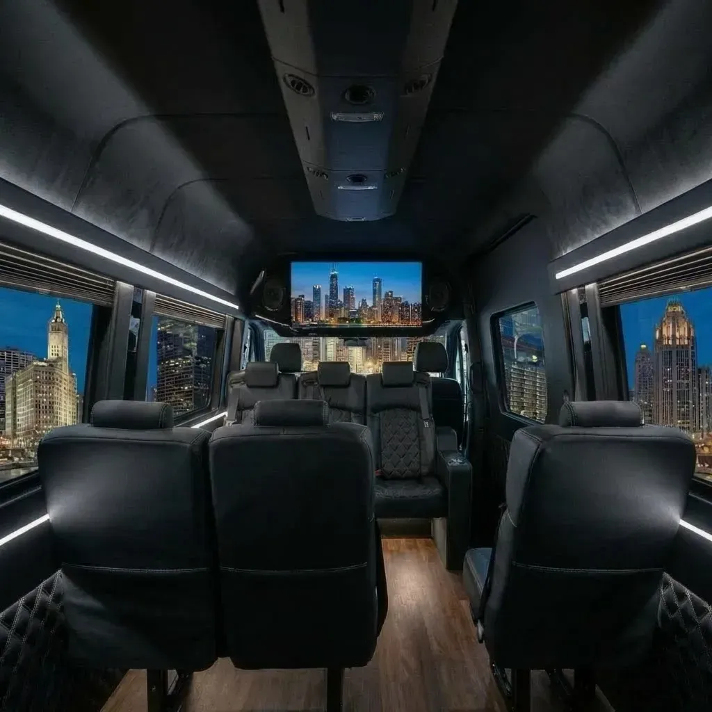 Interior of a black luxury van with leather seats, a TV, and a cityscape visible through the windows.