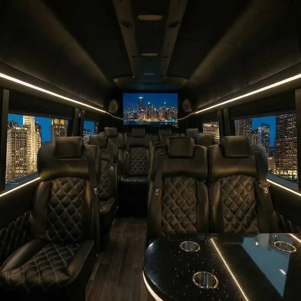 Interior of a luxury black party bus with leather seats, a large screen, and city views.