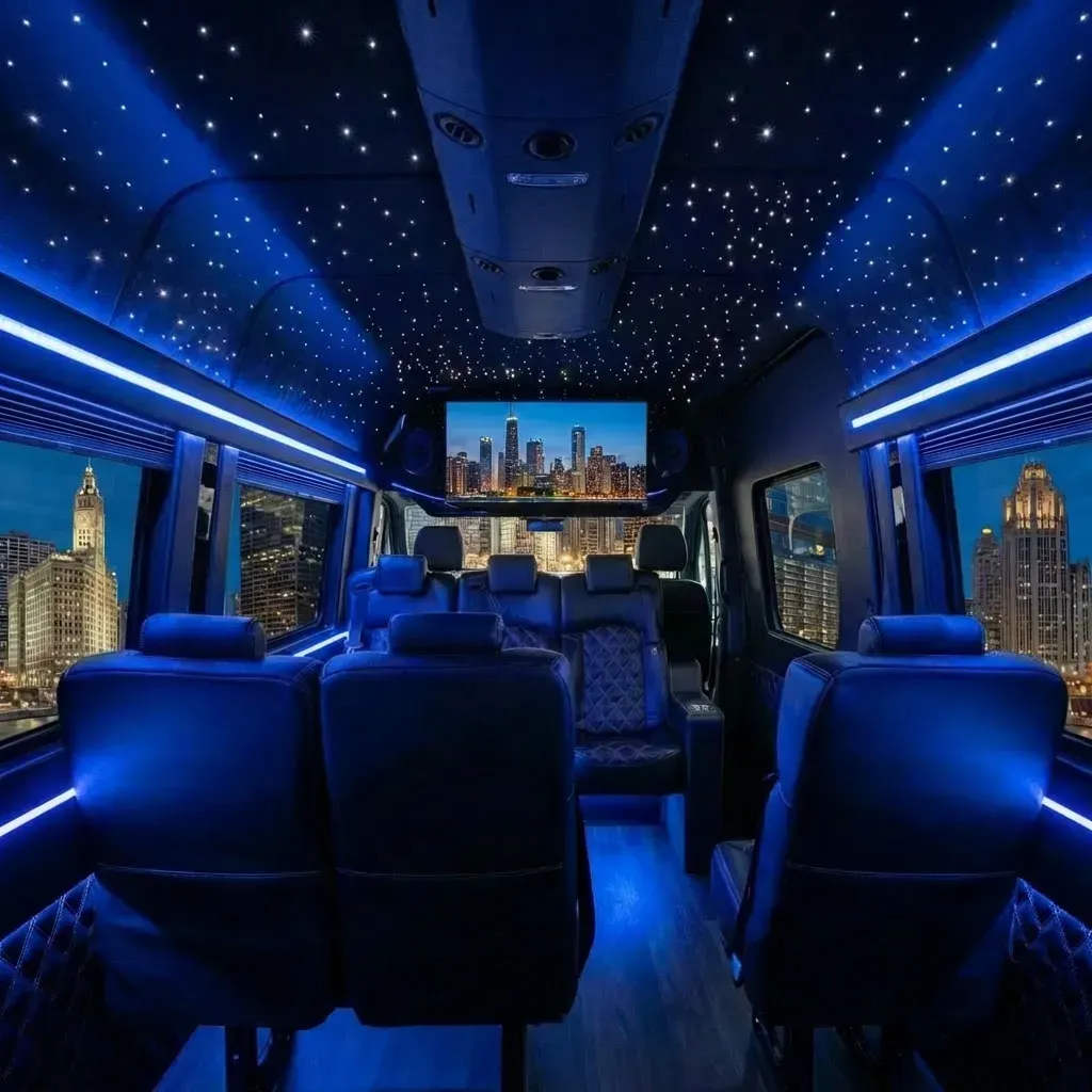 Interior of a luxury van with blue lighting, starry ceiling, leather seats, and a city view on a TV screen.