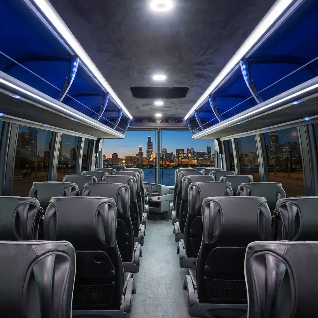 Interior of a bus with rows of black seats facing forward; windows reveal a cityscape at dusk.