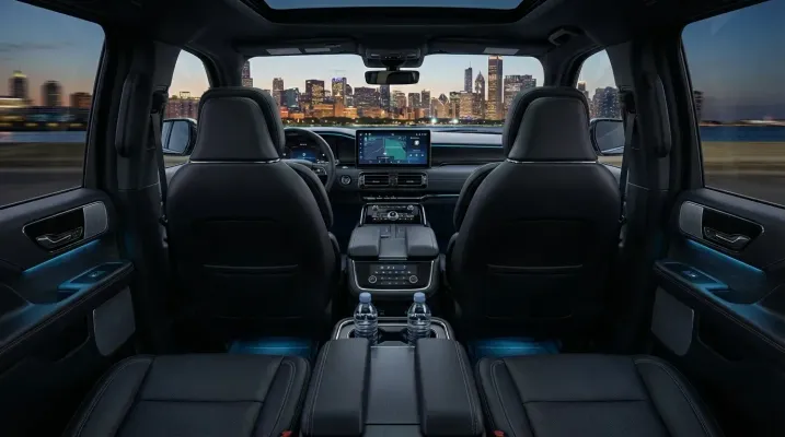 Interior of a vehicle with two rows of seats, illuminated by blue lights, with a city skyline visible through the windshield.