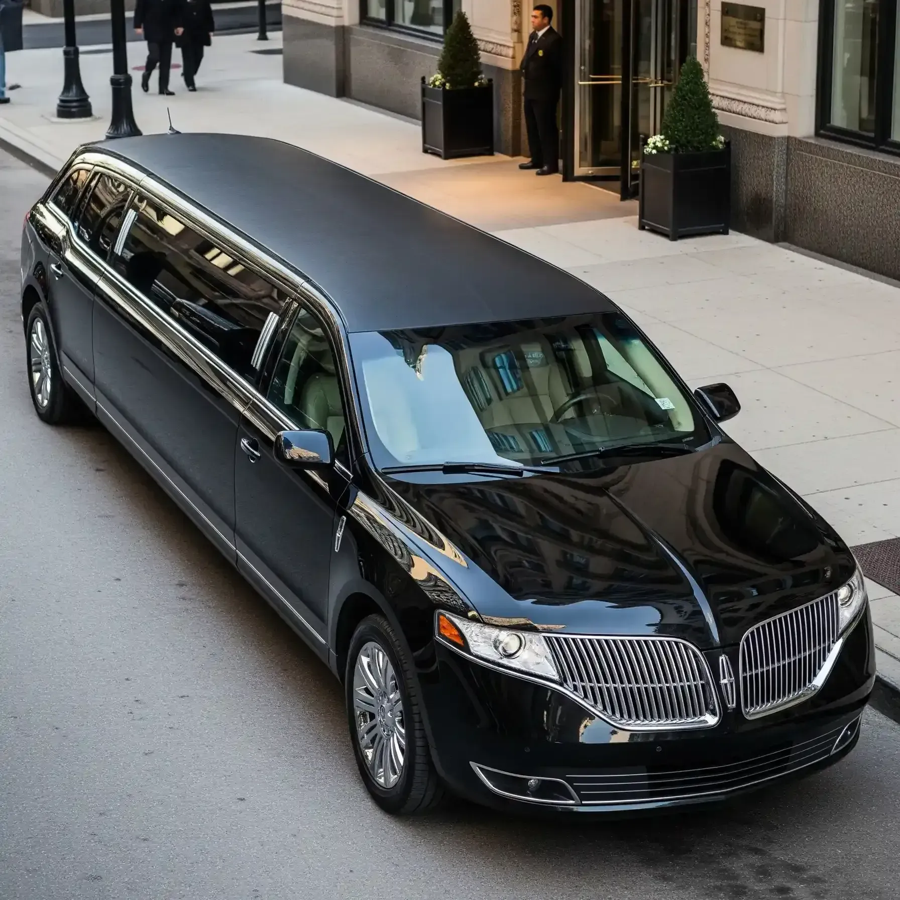 Black limousine parked in front of a building with a doorman; two people walk in the background.