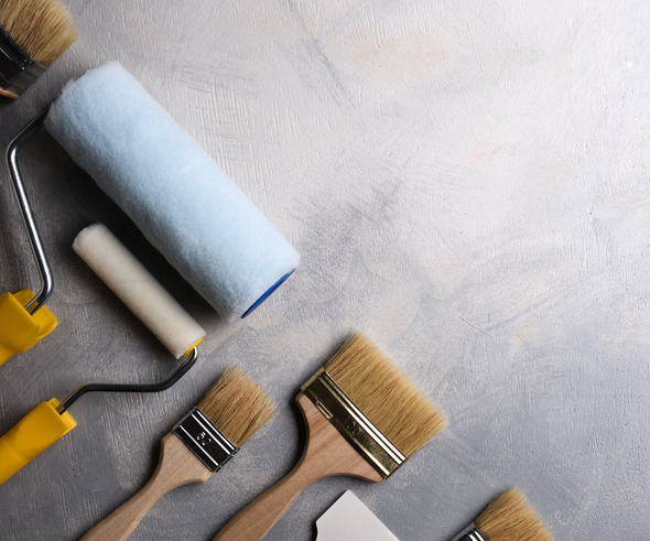 Paint roller and assorted paintbrushes on a gray surface, with a blue roller cover and yellow handles.