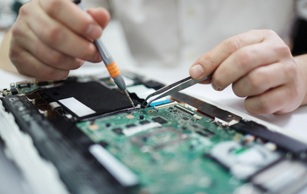 A person is working on a laptop with a screwdriver and tweezers.