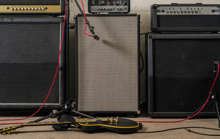 A guitar is sitting on the floor next to a bunch of amps.