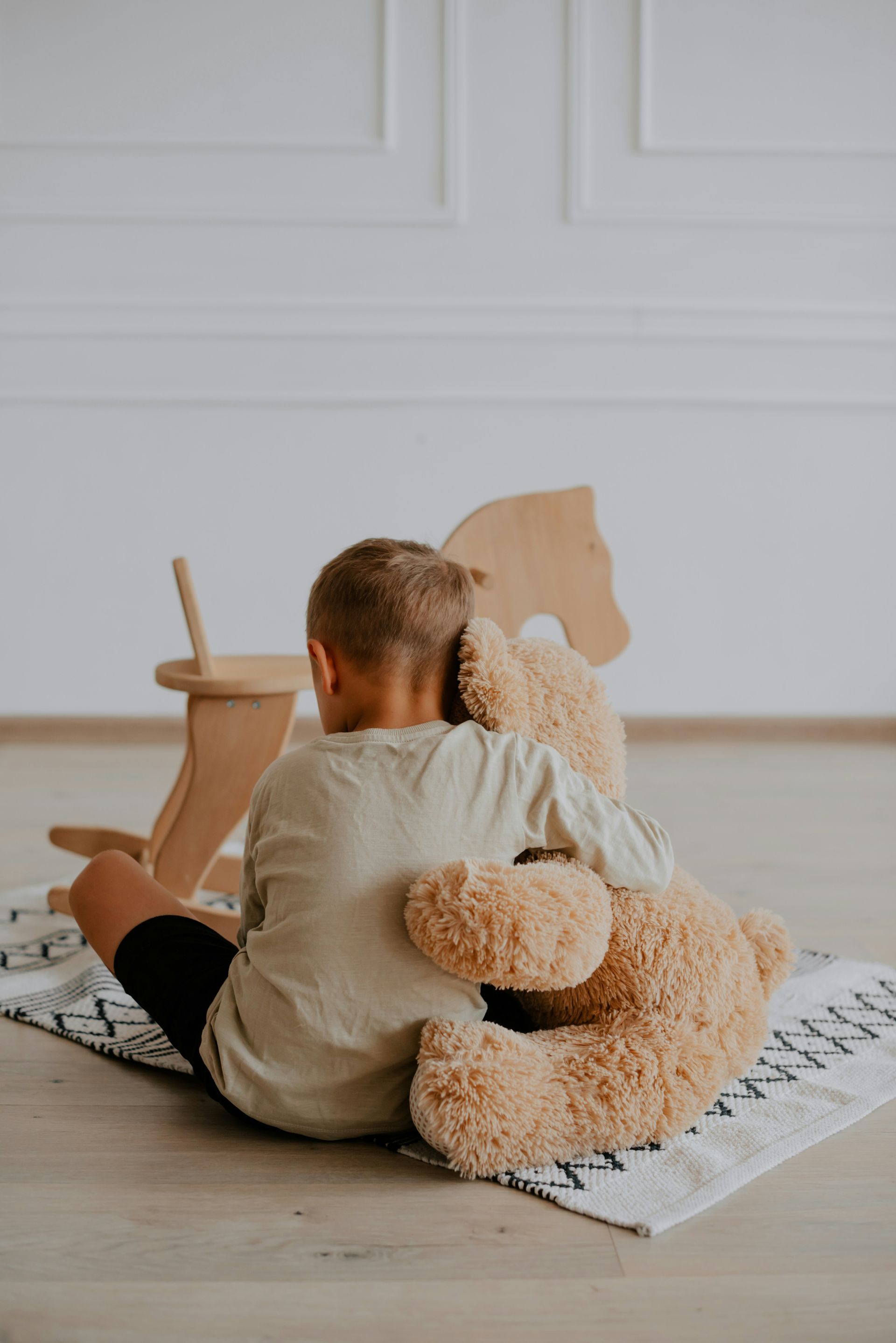 A young boy is sitting on the floor holding a teddy bear.