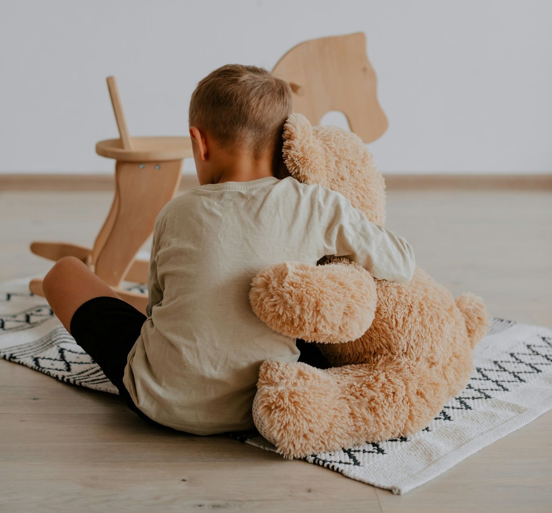 A young boy is sitting on the floor hugging a teddy bear