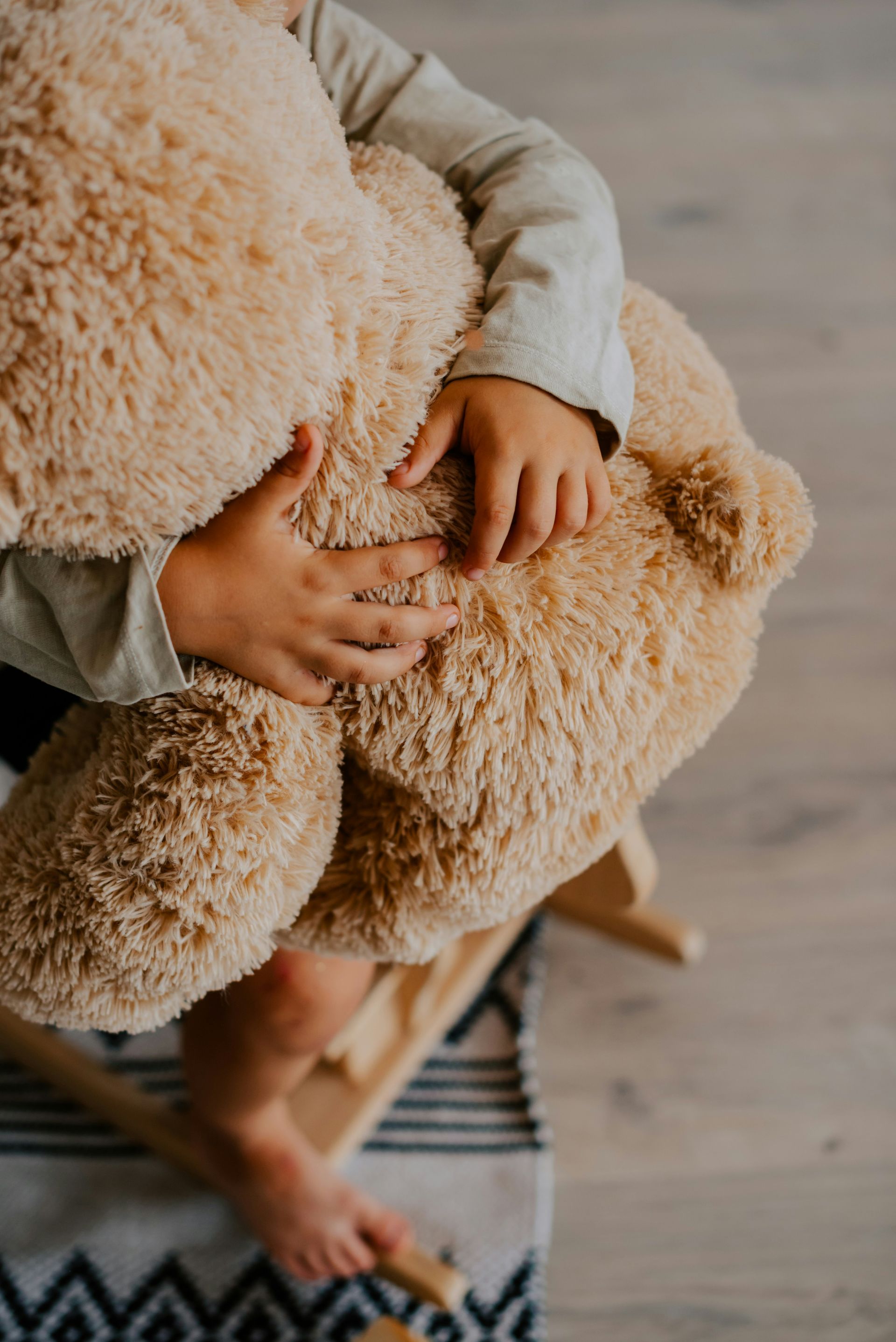 A child is holding a teddy bear while sitting on a rocking chair.