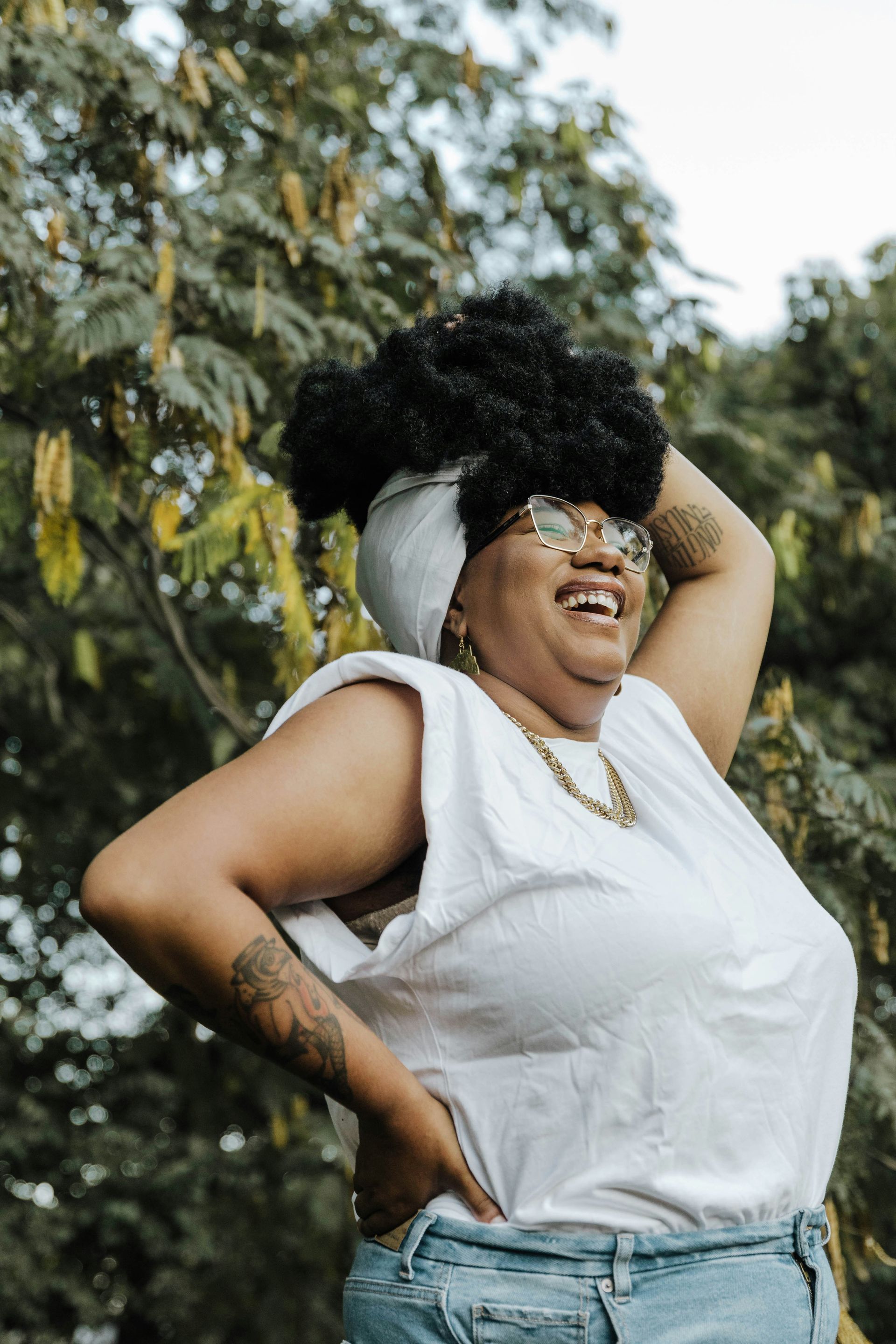 A woman wearing glasses and a white shirt is standing in front of a tree.