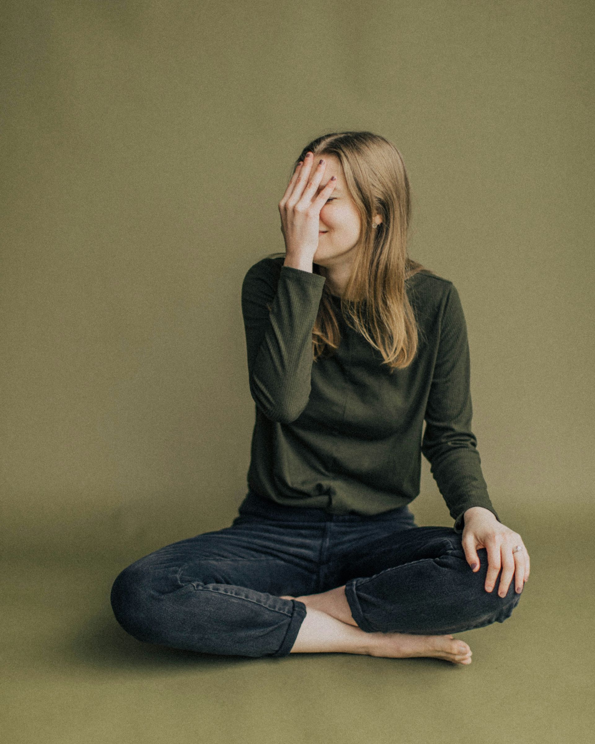 A woman is sitting on the floor covering her face with her hand.