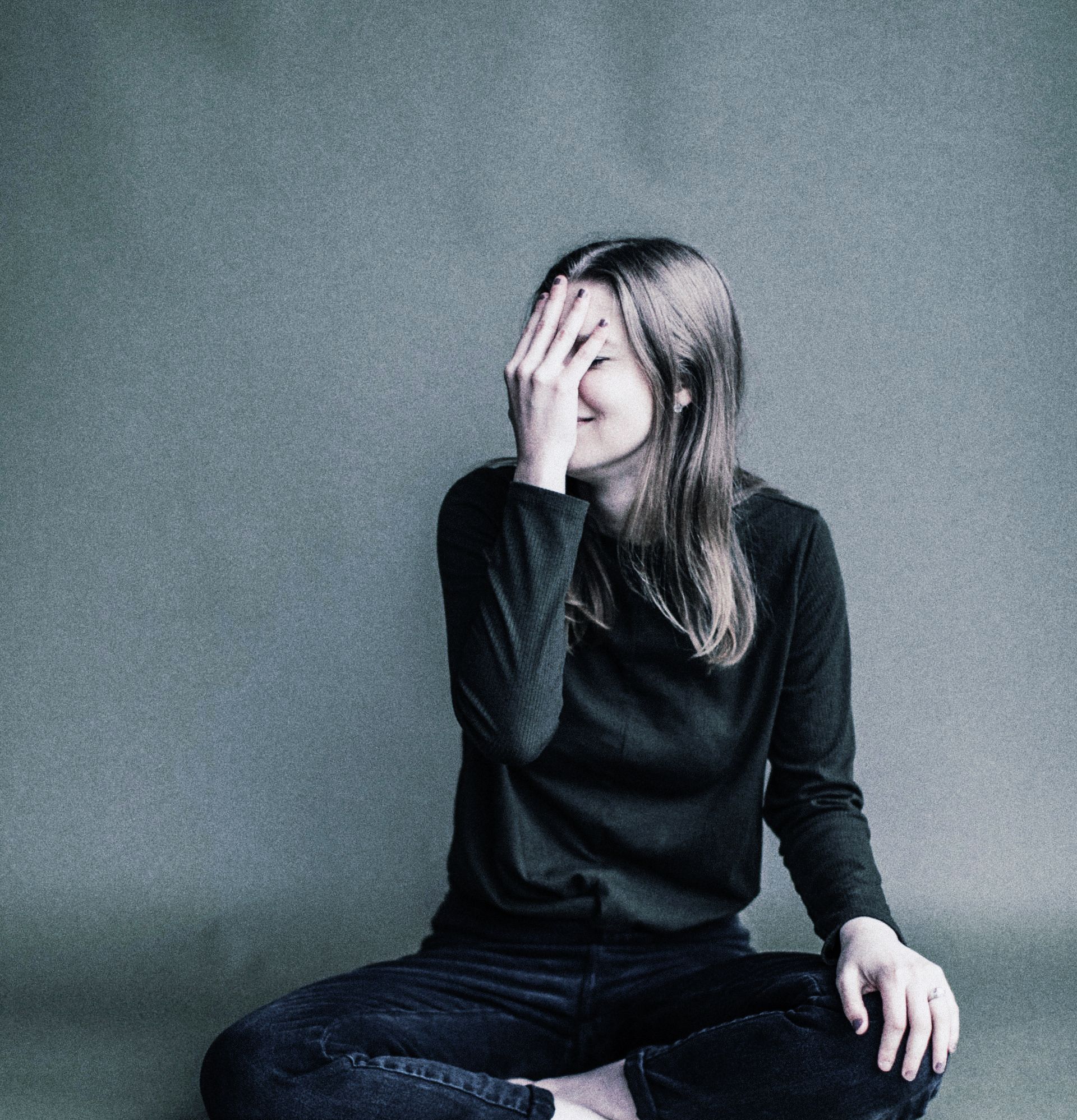 A woman is sitting on the floor covering her face with her hand