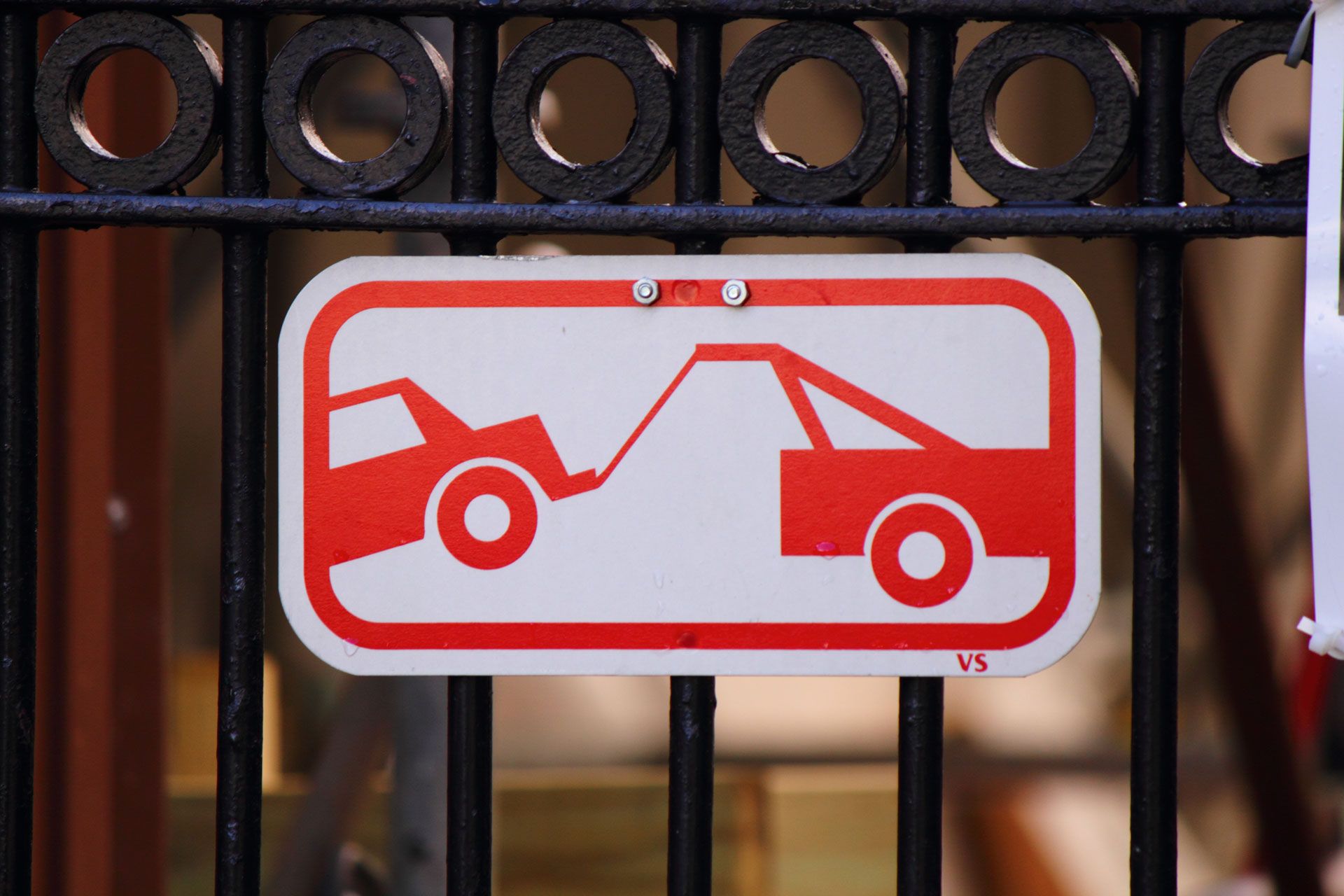Sign with red car being towed, against a white background; attached to black metal fence.